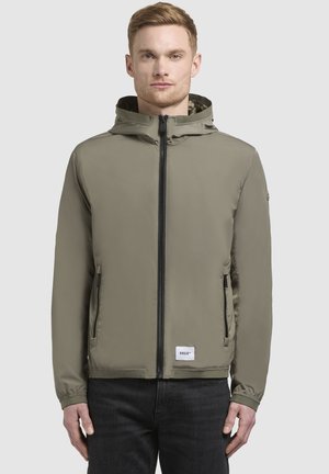 Kaki hættetrøje med frontlynlås, to sidelommer og elastiske manchetter. Har et logo-patch ved kanten og en glat tekstur.