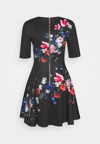 Robe noire à manches demi-longues, motif floral en rouge, rose et bleu. Fermeture éclair au dos, design de jupe évasée, matière lisse.