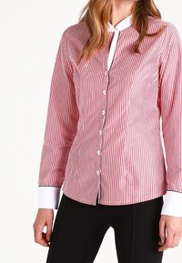Camisa de botones a rayas rojas y blancas con mangas largas, cuello y puños blancos, diseño ajustado y textura de tela suave.