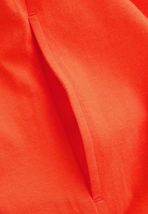 Tessuto arancione brillante con una superficie liscia presenta un'apertura per una tasca laterale. Il design complessivo è semplice e contemporaneo.