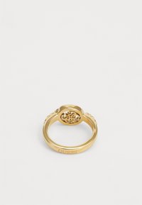 Χρυσόχρωμο μεταλλικό δαχτυλίδι με σχεδίαση κομμένου λογότυπου και διακοσμητικά στοιχία πάνω στην ταινία. Χαραγμένο «GUESS» στο εσωτερικό.