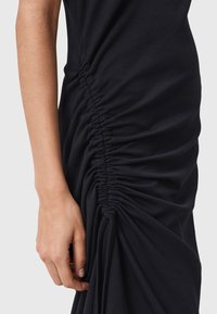 Abito nero con texture arricciata lungo il lato, che mostra un tessuto morbido e un design aderente, con un primo piano di una mano che tiene il capo.