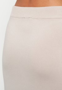 Jupe en tissu extensible beige clair avec une texture lisse et une taille élastique. Vue en gros plan mettant l'accent sur le matériau et la couleur.