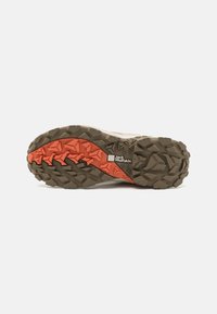Terrenglsertsåle med teksturert brun gummi med oransje detaljer, robuste spor for grep, og en fremtredende logo på siden.