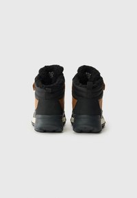 Botines marrones y negros con parte superior texturizada, forro de piel sintética y suelas de goma. Cuenta con una lengüeta y un collar acolchado para mayor comodidad.