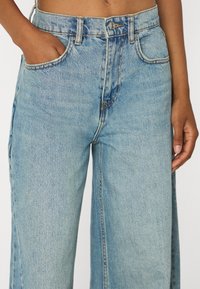 Svetlomodré džíny s širokými nohavicami a vysokým pásom, so zapínaním na gombík a zips, piatimi vreckami a viditeľnými švami.