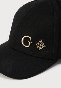 Μαύρο καπέλο από ύφασμα με μίγμα μαλλιού· διαθέτει χρυσό λογότυπο "G" και χρυσό έμβλημα σε σχήμα ρόδου του ανέμου κοντά στην άκρη.