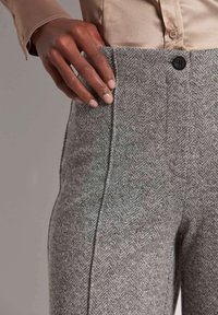 Grijze herringbone broek met een gestructureerde afwerking. Bevat een zwarte knoop en zijzak, gecombineerd met een lichtbeige blouse.