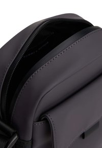 Bolso cruzado estructurado en material gris oscuro. Presenta una textura suave, cierre de cremallera y costuras en contraste a lo largo de los bordes.