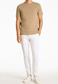 Krótka koszulka z krótkim rękawem w kolorze beżowym z okrągłym dekoltem, zestawiona z białymi, dopasowanymi spodniami i białymi trampkami, o gładkiej fakturze.