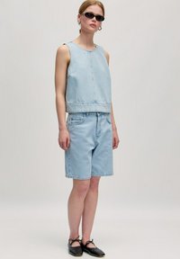 Lichtblauw denim cropped tanktop gecombineerd met lichtblauwe denim shorts. Accessoires zijn onder andere zwarte ovale zonnebril en platte zwarte schoenen met veters.