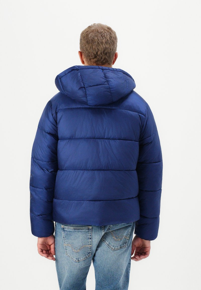 Navyblaue Daunenjacke mit abnehmbarem Kapuze, gestepptem Muster und elastischen Bündchen, kombiniert mit hellblauen Jeans.