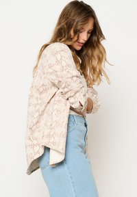 Beige snake-print shirt with rolled sleeves, lightweight material, and a slightly longer back, paired with light blue jeans.