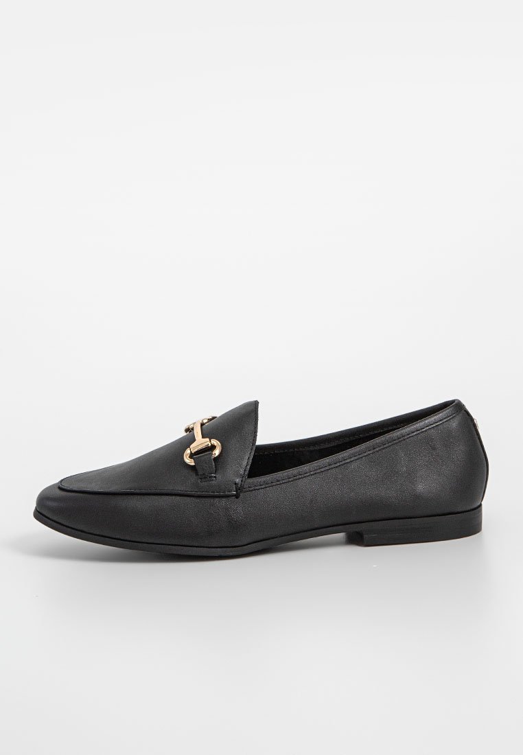 Mocasines de cuero negro con suela plana, que presentan un acento metálico dorado en la parte delantera. Textura suave y forma alargada.