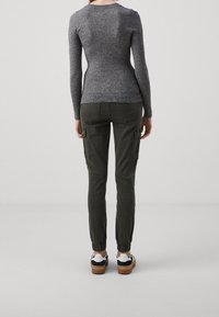 Un pull gris à rayures avec des manches longues associé à un pantalon cargo vert olive comportant des poches latérales et des poignets élastiques, complété par des baskets blanches et bleu marine.