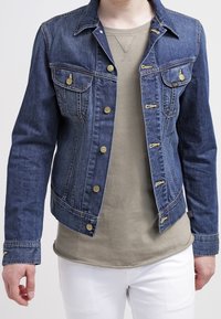 Donkerblauwe denimjack met een getailleerd ontwerp, voorzien van gouden knopen, twee borstzakken en een kraagachtige halslijn. Witte onderhemd zichtbaar.