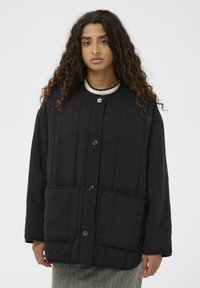 Črna prešita jakna z visokim ovratnikom, sprednjimi žepi in zapiranjem na gumbe. Tkanina ima teksturo z vertikalnimi šivi.