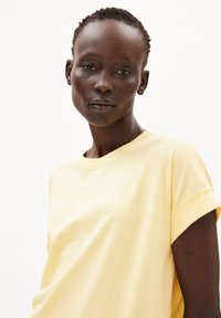 T-shirt giallo a maniche corte realizzato in un morbido tessuto, con un piccolo logo in rilievo sulla parte anteriore. Il collo è a girocollo con maniche arrotolate.