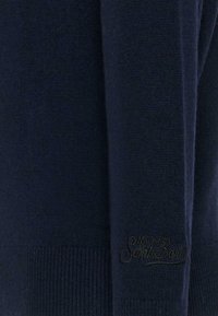 Granatowy sweter z miękkiej mieszanki wełny, z prążkowanymi mankietami i subtelnym haftowanym logo na dolnym brzegu. Gładka tekstura z minimalnymi detalami.