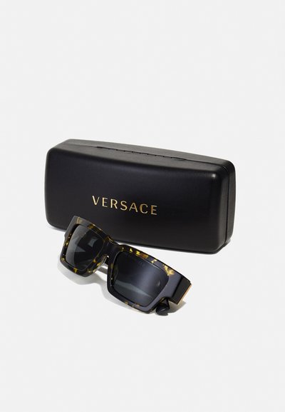 Svart og skilpadde solbriller med firkantede glass, plassert i et svart etui med gull "VERSACE"-merking på forsiden.