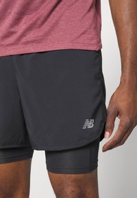 Schwarze Sportshorts mit schichtartigem Design, aus leichtem Material und mit einem dezenten New Balance Logo auf der linken unteren Seite.