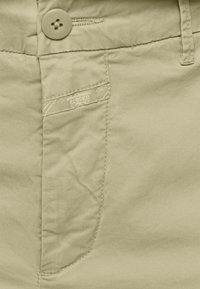 Ljust beige bomullsbyxor med knappstängning, framficka med diskret sömnad och en slät, texturerad tyg.