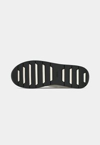 Semelle de chaussure avec un motif en caoutchouc noir et blanc présentant de profondes rainures horizontales et le logo "BOSS" au centre.