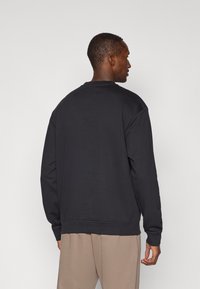 Schwarzer Pullover mit rundem Ausschnitt, lockerer Passform, gerippten Bündchen und Saum, aus weichem Material gefertigt. Von hinten mit neutralem Hintergrund gezeigt.