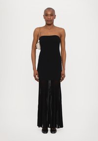 Black strapless dress with a fitted bodice and a pleated chiffon skirt. Model holds a small handbag. Black shoes complete the look.