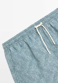 Shorts de bain teal avec un motif zigzag blanc, dotés d'une taille élastique et d'un cordon de serrage pour l'ajustement. Texture de tissu léger.