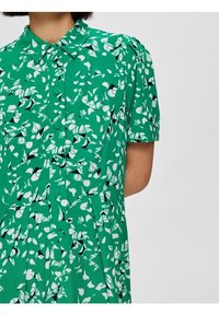 Vestito verde con bottoni, caratterizzato da un motivo a foglie in bianco e nero, maniche corte, colletto e dettagli plissettati sul gonnellino.