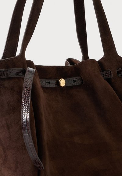 Sac cabas en daim marron foncé avec deux anses, doté d'une bandoulière en cuir sombre texturée et d'un petit bouton rond doré à l'avant.