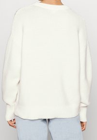 Witte geribbelde trui met een losse pasvorm, met lange mouwen en een brede halslijn, gezien van achteren tegen een effen achtergrond.