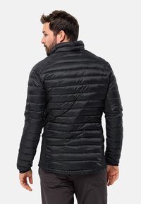 Sort pufferjakke med vandrette quiltede sektioner, høj krave og et sleek design, sammen med mørke bukser og en neutral baggrund.