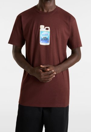 Mand iført en mørkerød t-shirt med en grafik af en hvid og blå flaske mærket "Vans Liquid Off The Wall" på fronten.