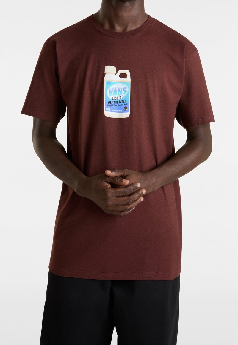 Homme portant un t-shirt bordeaux avec un graphisme d'une bouteille blanche et bleue étiquetée "Vans Liquid Off The Wall" sur le devant.