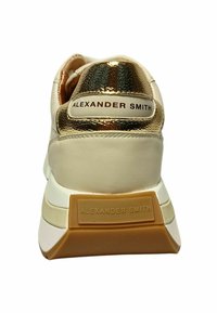 Witte en gouden sneaker met een glad leren bovenwerk, metallic gouden accenten op de hak en een gestructureerde rubberen zool met merknaam details.
