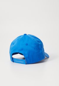 Blauwe katoenen baseballcap met een gebogen rand, verstelbare snapback en een "Calvin Klein" label op de band. Glad van textuur en een eenvoudig ontwerp.