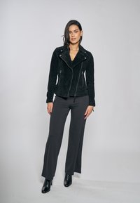 Černá semišová motorkářská bunda s přiléhavým střihem, zapínáním na zip a bočními kapsami, doplněná tmavými širokými kalhotami a černými botami na podpatku.