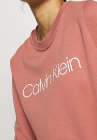 Felpa di cotone rosa con scollo rotondo e logo bianco "Calvin Klein" sul davanti. Tessuto morbido, design casual.