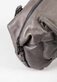 Borsa in pelle grigia con finitura testurizzata, dotata di una cerniera superiore e spallacci regolabili. Include cuciture delicate e un piccolo etichetta decorativa.