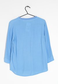 Helles blaues Langarmshirt mit Rundhalsausschnitt, weichem Material und abgerundetem Saum. Mit hochrollbaren Ärmeln und einem Etikett auf der Rückseite.