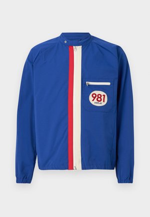 Veste zippée bleue avec des rayures verticales rouges et blanches, poche poitrine zippée et patch "981 REPLAY" sur la poche.