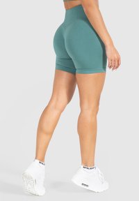 Shorts de sport taille haute, en teal, avec une texture côtelée, un design ajusté et une longueur mi-cuisse, associés à des baskets blanches et des chaussettes.