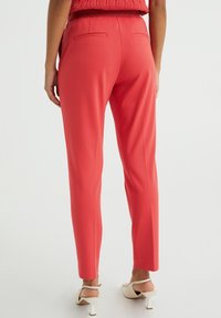 Red trousers with a slim fit, featuring side pockets and a comfortable waistband. Paired with light-colored, block-heeled shoes.