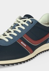 Baskets bleu marine avec lacets blancs, accents de bandes rouges, semelle blanche et logo "BOSS" sur le côté et la languette.