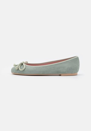 Groene suède ballerina met ronde neus, decoratieve koordstrik aan de voorkant en beige rubberen zool, zijaanzicht op een witte achtergrond.