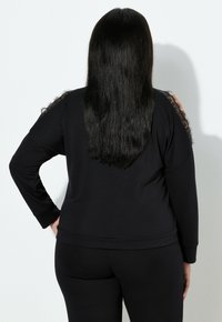 Maglione nero a maniche lunghe, con dettagli in pizzo trasparente sulle spalle e una vestibilità rilassata, abbinato a pantaloni neri coordinati.