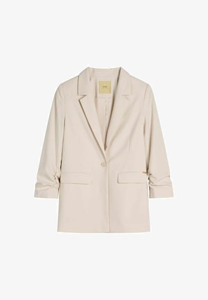 Beżowa damska marynarka z klapami z wycięciem, zapinana na jeden guzik, z dwoma przednimi kieszeniami z patkami oraz marszczonymi rękawami o długości trzy czwarte.