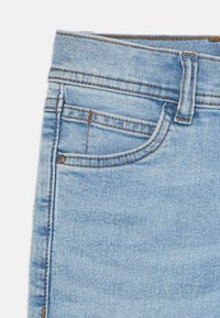 Κοντινή λήψη μπλε τζιν μεσαίου φωτός που δείχνει την μπροστινή τσέπη, τη μικρή τσέπη για κέρματα, το θηλύκι της ζώνης και τις ορατές λεπτομέρειες ραφής.